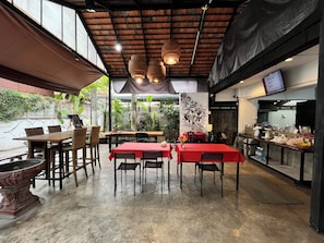 A restaurant with a high ceiling, exposed beams, and large windows. Tables are covered with red tablecloths, and there are wicker chairs. - Rcn Court (Chiang Mai)