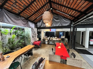 An indoor dining area with a high ceiling, tables with red and white tablecloths, wicker chairs, and a central hanging light fixture. - Rcn Court (Chiang Mai)