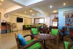 A spacious living room with a high ceiling, a television mounted on the wall, a bookshelf, and a window with blinds. - Rcn Court (Chiang Mai)
