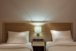 Una habitación de hotel con dos camas, una mesita de noche, una lámpara fijada a la pared y un cabecero de madera.