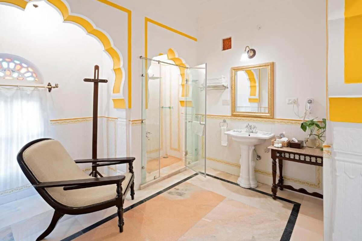 A bathroom with a glass shower enclosure, a white sink with a mirror, and a chair.