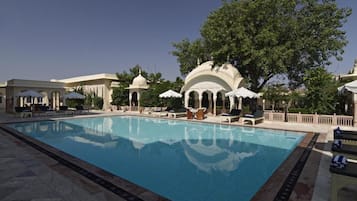 A swimming pool with lounge chairs and umbrellas, surrounded by white buildings with domed structures.