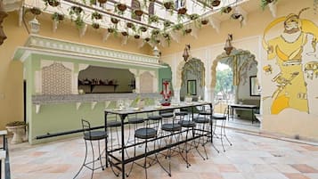 A dining area with a long table and chairs, a decorative wall with a mural, hanging plants, and a traditional architectural style.