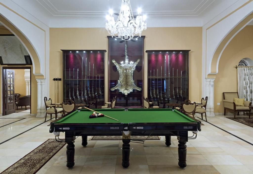 A pool table in a spacious room with a chandelier, large windows with curtains, and classic furniture.