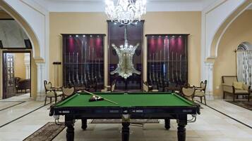 A pool table in a spacious room with a chandelier, large windows with curtains, and classic furniture.