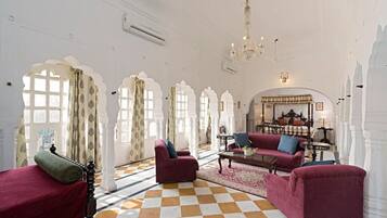 A spacious room with a checkered floor, red armchairs, a coffee table, and a chandelier.