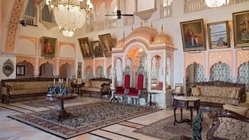 A grand lobby with ornate chandeliers, traditional sofas, and a large patterned rug.