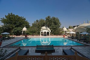 A swimming pool with a pavilion, lounge chairs, and potted plants. - Alsisar Mahal- Heritage Palace Hotel (Malasisar)