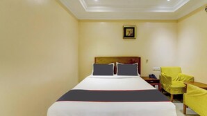 A hotel room with a bed, a chair, a nightstand, and a painting on the wall. - Rg Suites Ashok Nagar (Chennai)