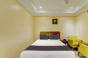 A hotel room with a bed, a chair, a nightstand, and a painting on the wall. - Rg Suites Ashok Nagar (Chennai)