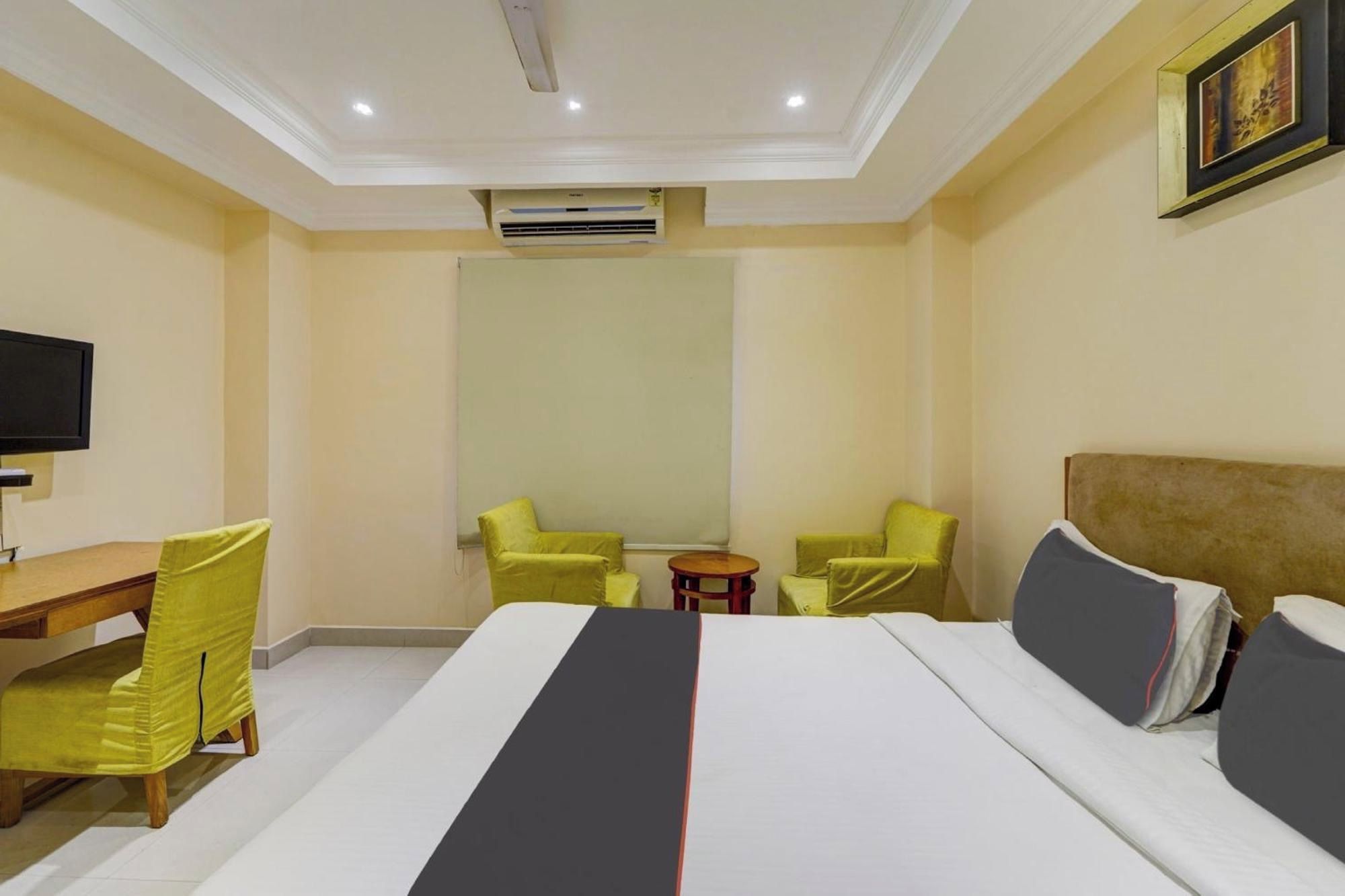 A hotel room with a bed, a desk, two chairs, a small table, and a television.