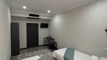 A hotel room with two single beds, a desk with a chair, a small table, and a TV on the wall.