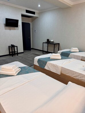 A hotel room with three beds, a small table with a phone, a TV mounted on the wall, and a door.