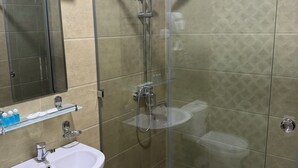A modern bathroom with a glass-enclosed shower, a white pedestal sink, and a glass shelf with toiletries. - Mehran (Fergana)