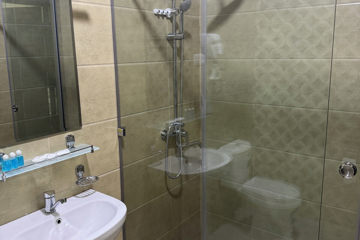 Et moderne badeværelse med en glasafskærmet brusekabine, en hvid konsolvask og en glashylde med toiletartikler.