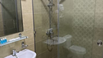 Ein modernes Badezimmer mit einer einachigen Duschkabine, einem weißen Waschbecken auf Säule und einem Glastablett mit Pflegeprodukten.