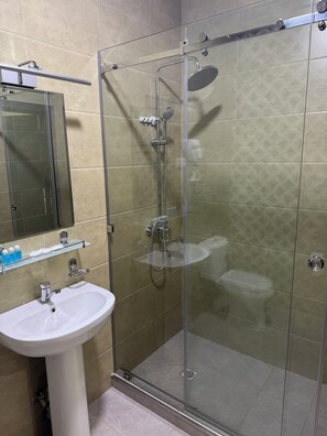 Et moderne badeværelse med en glasafskærmet brusekabine, en hvid konsolvask og en glashylde med toiletartikler.