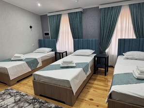 Een hotelkamer met drie eenpersoonsbedden, een kleine tafel en een televisie.