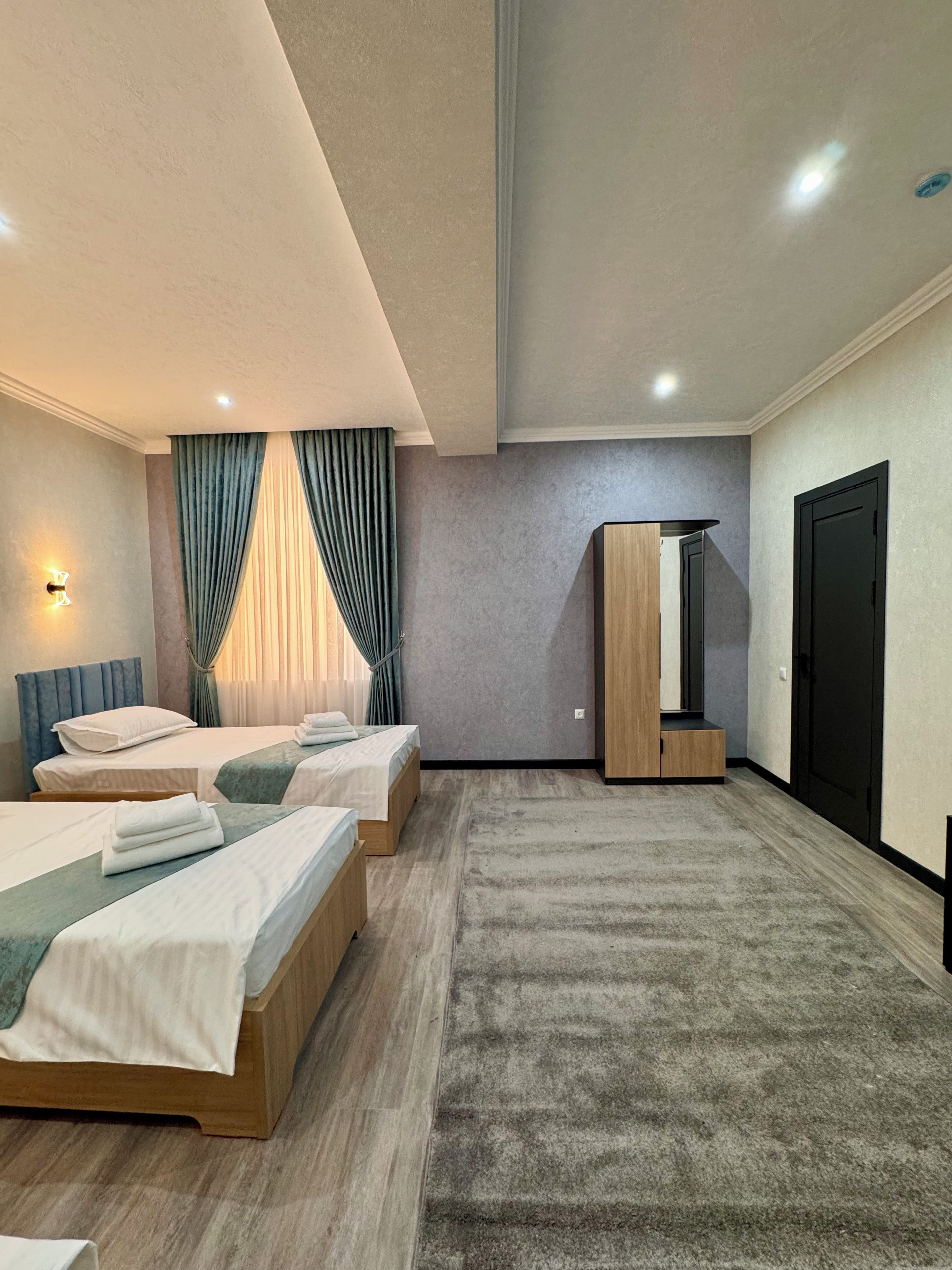 Una habitación de hotel moderna con dos camas, un espejo grande, un armario y piso alfombrado.