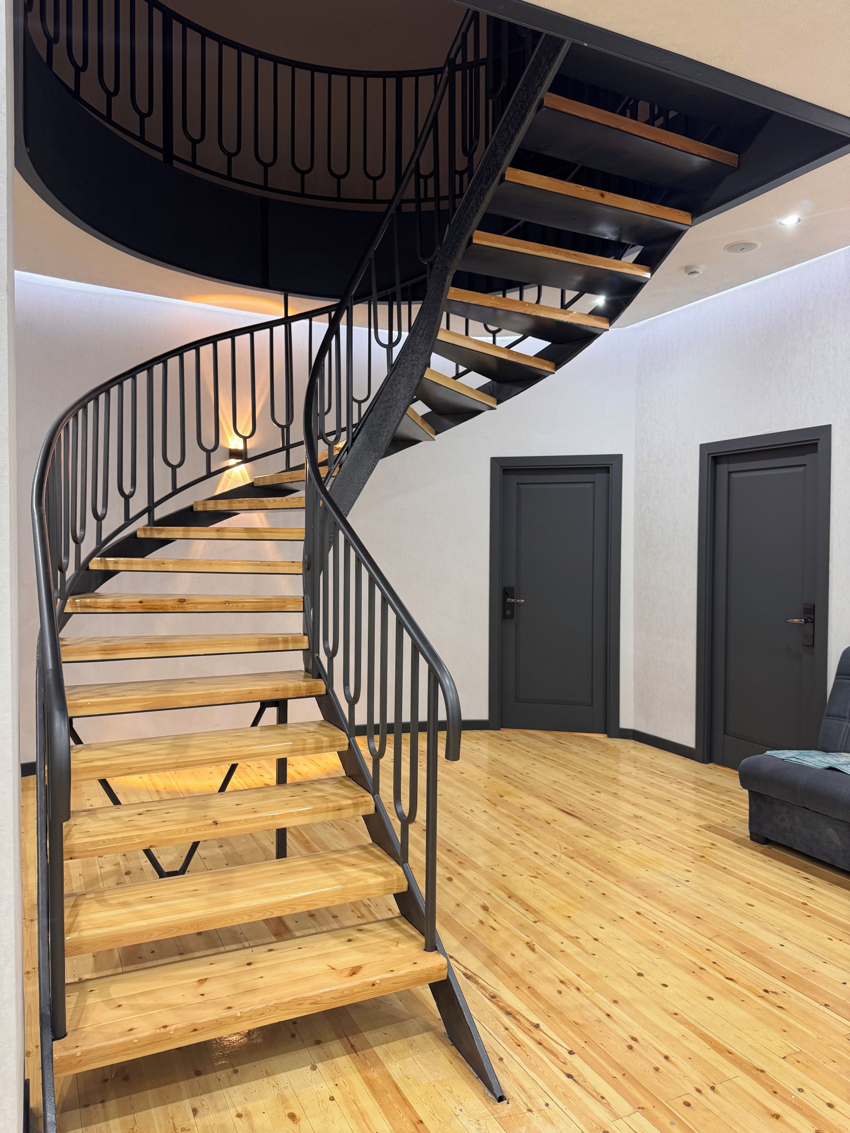Una escalera en espiral con escalones de madera y barandillas de metal negro que conduce a un piso superior.