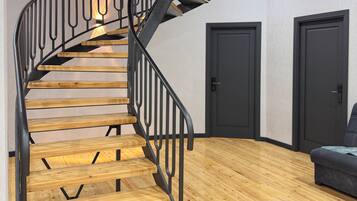 Una escalera en espiral con escalones de madera y barandillas de metal negro que conduce a un piso superior.