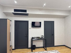 A modern room with two dark doors, a mounted TV, a small table with a kettle, and a trash bin. - Mehran (Fergana)