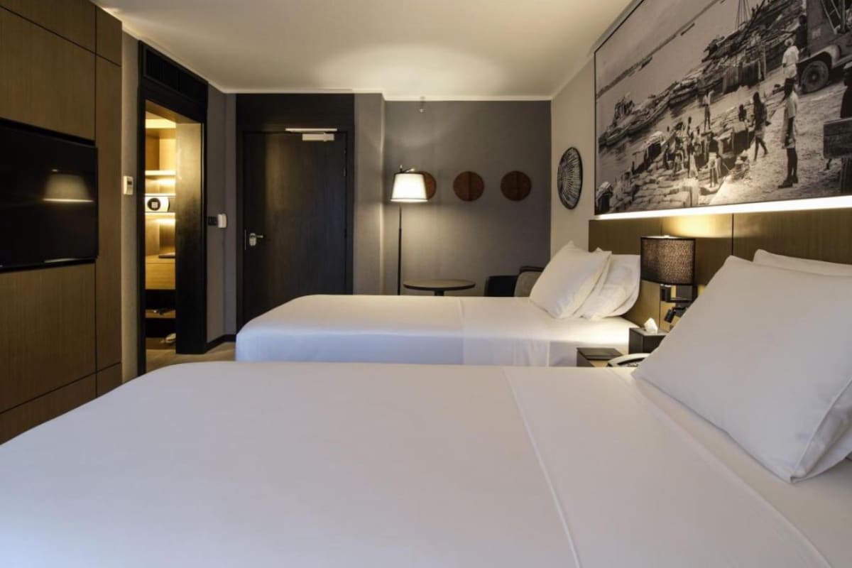 Camera d'albergo con due letti, una televisione, un quadro e una lampada.