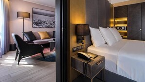 Hotellihuone, jossa on sänky, yöpöytä, lamppu ja sohva, jossa on koristetyynyjä.