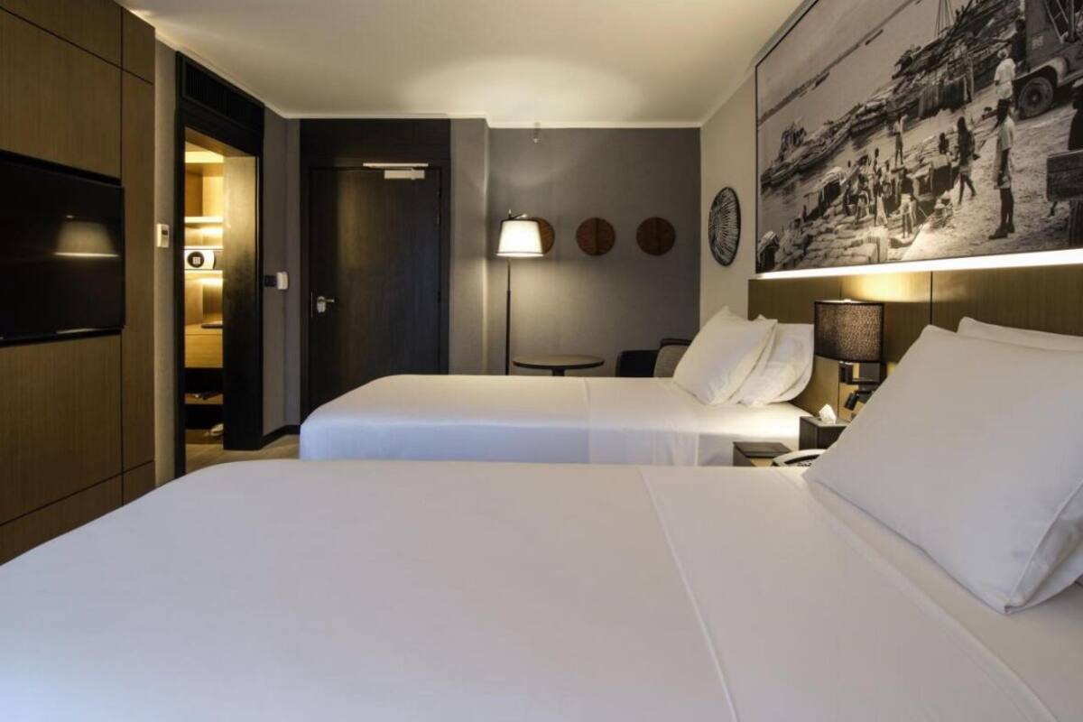 A hotel room with two beds, a television, a painting, and a lamp.