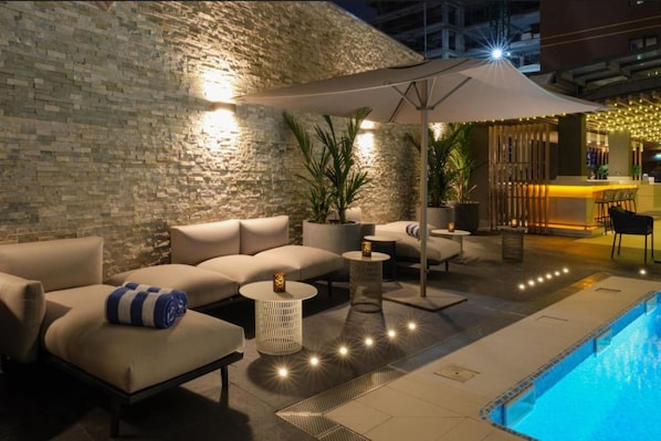 Area piscina esterna con muro in pietra, sedute relax e zona bar.