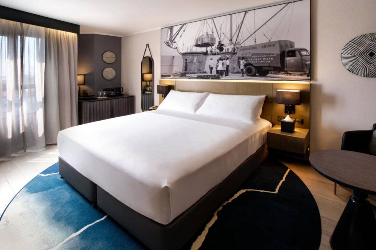 A modern hotel room with a large bed, a desk, a chair, and a dining table.