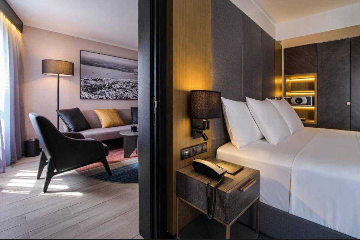 A hotel room with a bed, bedside table, lamp, and a sofa with cushions.