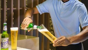 En person skænker øl i et glas i en bar, med en flaske og et glas øl på disken.