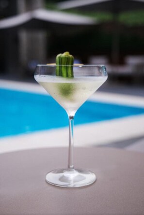 A martini glass with a green garnish on a table by a pool. - K Hotels (Douala)
