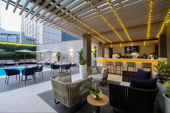 An outdoor lounge area with wicker furniture, a pool, and a bar with a 'K' logo. - K Hotels (Douala)