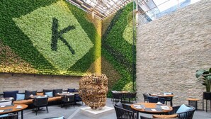 A restaurant with a green wall and a stone wall, featuring outdoor seating and a large sculpture. - K Hotels (Douala)