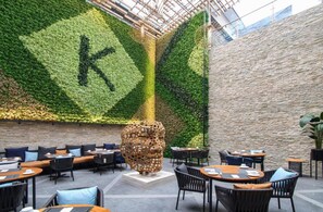 A restaurant with a green wall and a stone wall, featuring outdoor seating and a large sculpture. - K Hotels (Douala)