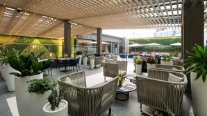 An outdoor seating area with wicker furniture, potted plants, and umbrellas. - K Hotels (Douala)