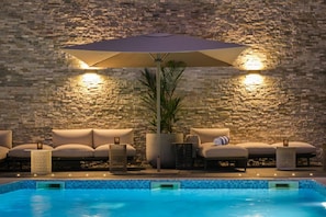 Area piscina con muro in pietra, un ombrellone grande e poltrone da relax.