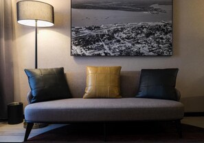 En moderne sofa med tre hynder i et rum med en lampe og et bybillede på væggen.