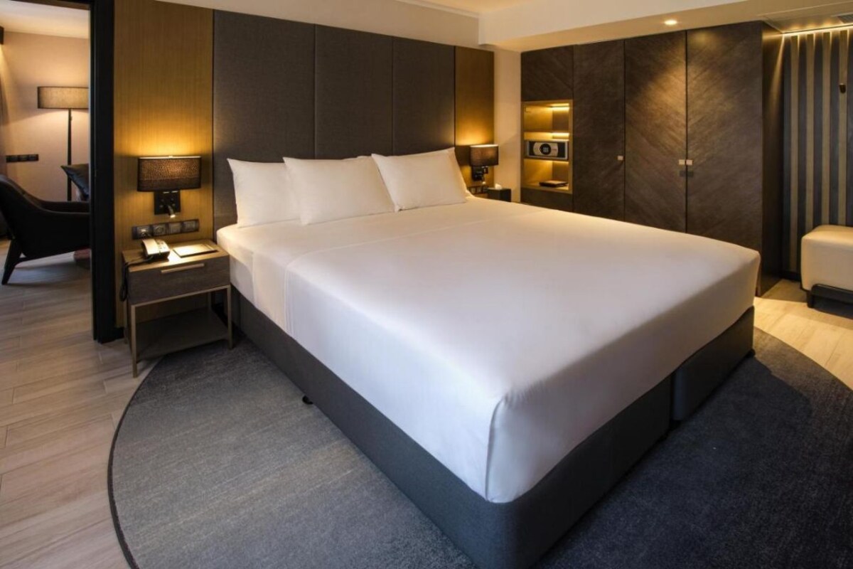 Une chambre d’hôtel moderne dotée d’un grand lit, d’une table de chevet avec une lampe, d’une armoire et d’un coin salon comprenant une chaise et une petite table.