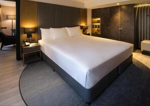 Et moderne hotelværelse med en stor seng, et sengebord med lampe, et garderobeskab og et siddeområde med stol og lille bord.