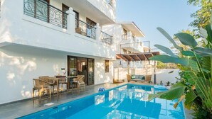 Un edificio moderno con piscina, mobiliario exterior y una zona cubierta.