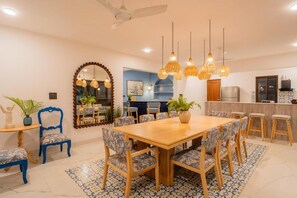 A dining area with a wooden table, patterned chairs, hanging lights, and a kitchen in the background. - Elivaas Paraíso - Villa Goa (Siolim)