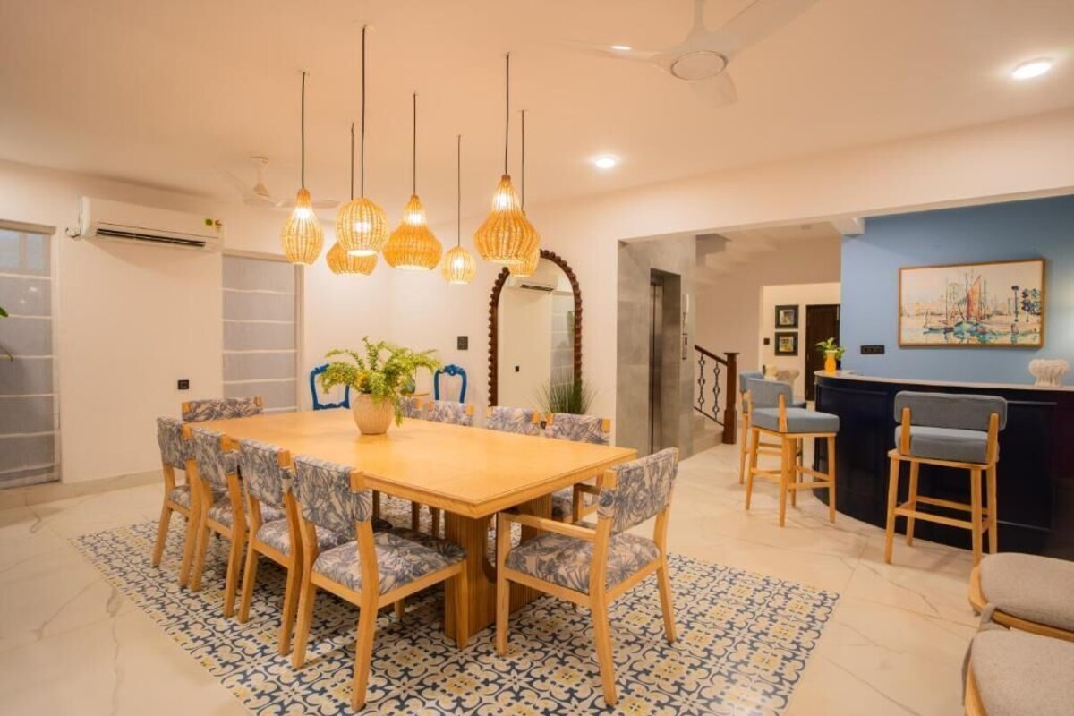 A dining area with a wooden table and chairs, hanging lights, and a patterned rug.