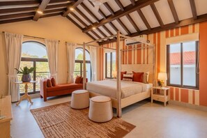 A bedroom with a four-poster bed, a sofa, two ottomans, and a nightstand with a lamp. - Elivaas Paraíso - Villa Goa (Siolim)