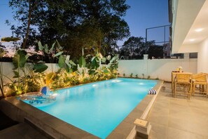 A swimming pool with a tiled deck, surrounded by tropical plants and a seating area with wicker furniture. - Elivaas Paraíso - Villa Goa (Siolim)