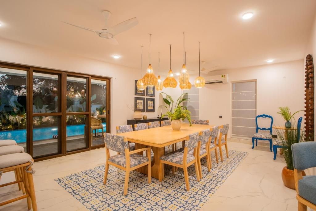 Un comedor con mesa de madera, sillas, luces colgantes y vista a una piscina.