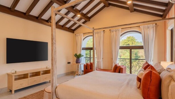Un dormitorio con cama con dosel, televisor de pantalla plana, una mesita con una planta y un balcón con cortinas.