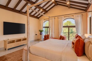 A bedroom with a four-poster bed, a flat-screen TV, a small table with a plant, and a balcony with curtains. - Elivaas Paraíso - Villa Goa (Siolim)